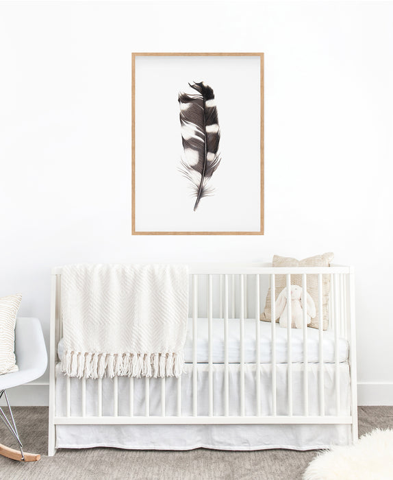 black and white feather colour pencil drawing in an oak frame hanging in a nursery above a white cot