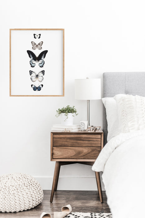 5 hand drawn butterflies in a timber frame hangign above a side table in a bedroom