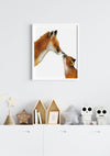 A drawing of a mama fox and her cub touching noses on a white background in a white frame hanging in a kids bedroom