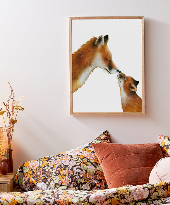 A drawing of a mama fox and her cub touching noses on a white background in a teak frame hanging in a bedroom above a bed