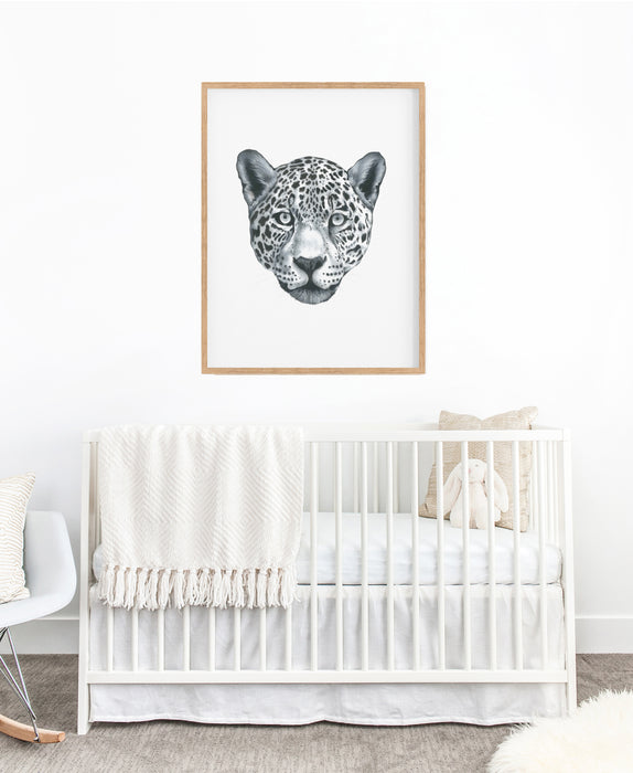 black and white drawing of leopards portrait in a timber frame hanging above a white cot in a nursery