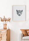 black and white illustration of a leopards portrait in a timber frame hanging above a lounge chair